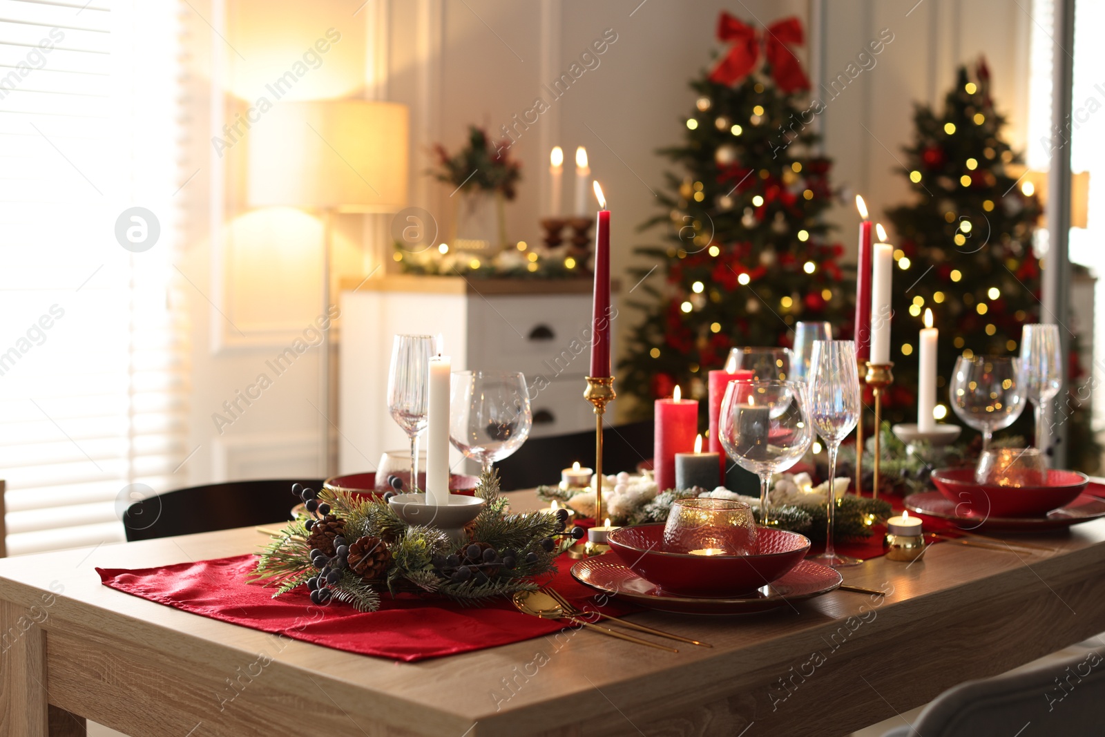 Photo of Christmas table setting with stylish dishware, glasses and burning candles in festive decorated room