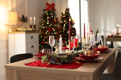 Photo of Christmas table setting with stylish dishware, glasses and burning candles in festive decorated room