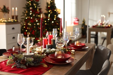 Photo of Christmas table setting with stylish dishware, glasses and burning candles in festive decorated room