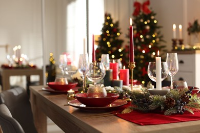 Photo of Christmas table setting with stylish dishware, glasses and burning candles in festive decorated room