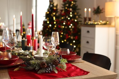 Photo of Christmas table setting with stylish dishware, glasses and burning candles in festive decorated room