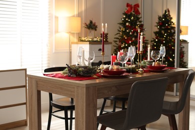 Photo of Christmas table setting with stylish dishware, glasses and burning candles in festive decorated room