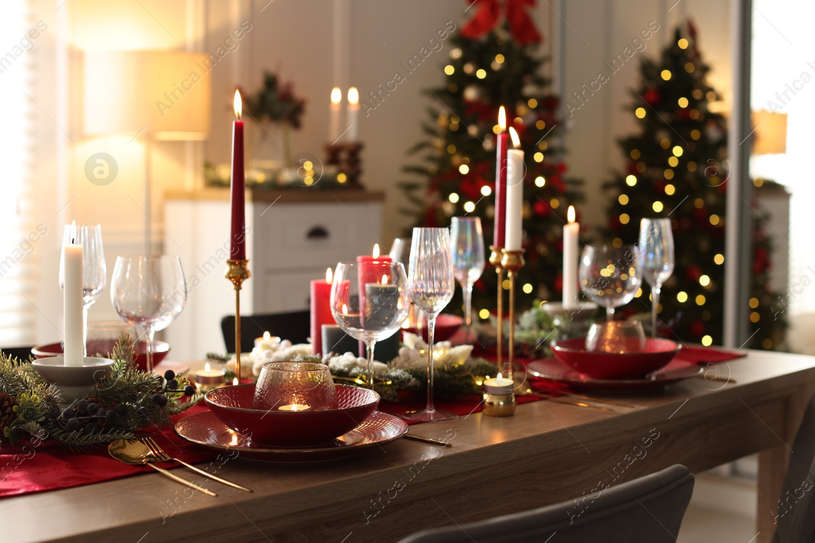 Photo of Christmas table setting with stylish dishware, glasses and burning candles in festive decorated room