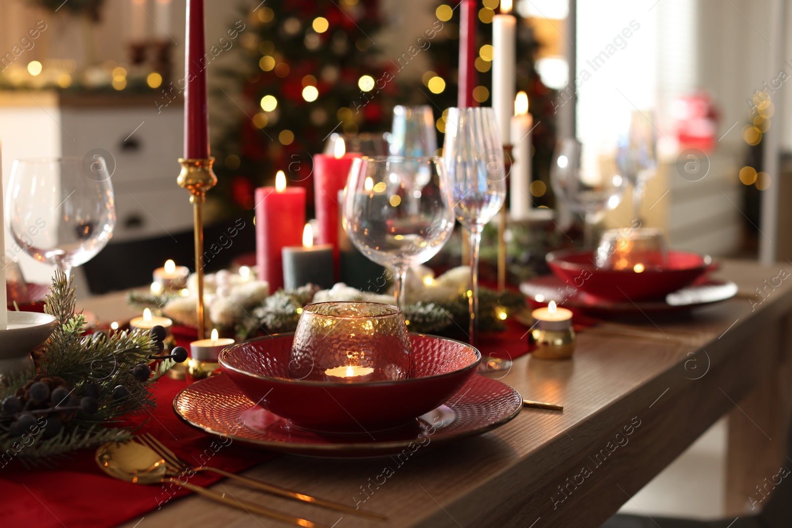 Photo of Christmas table setting with stylish dishware, glasses and burning candles in festive decorated room, closeup