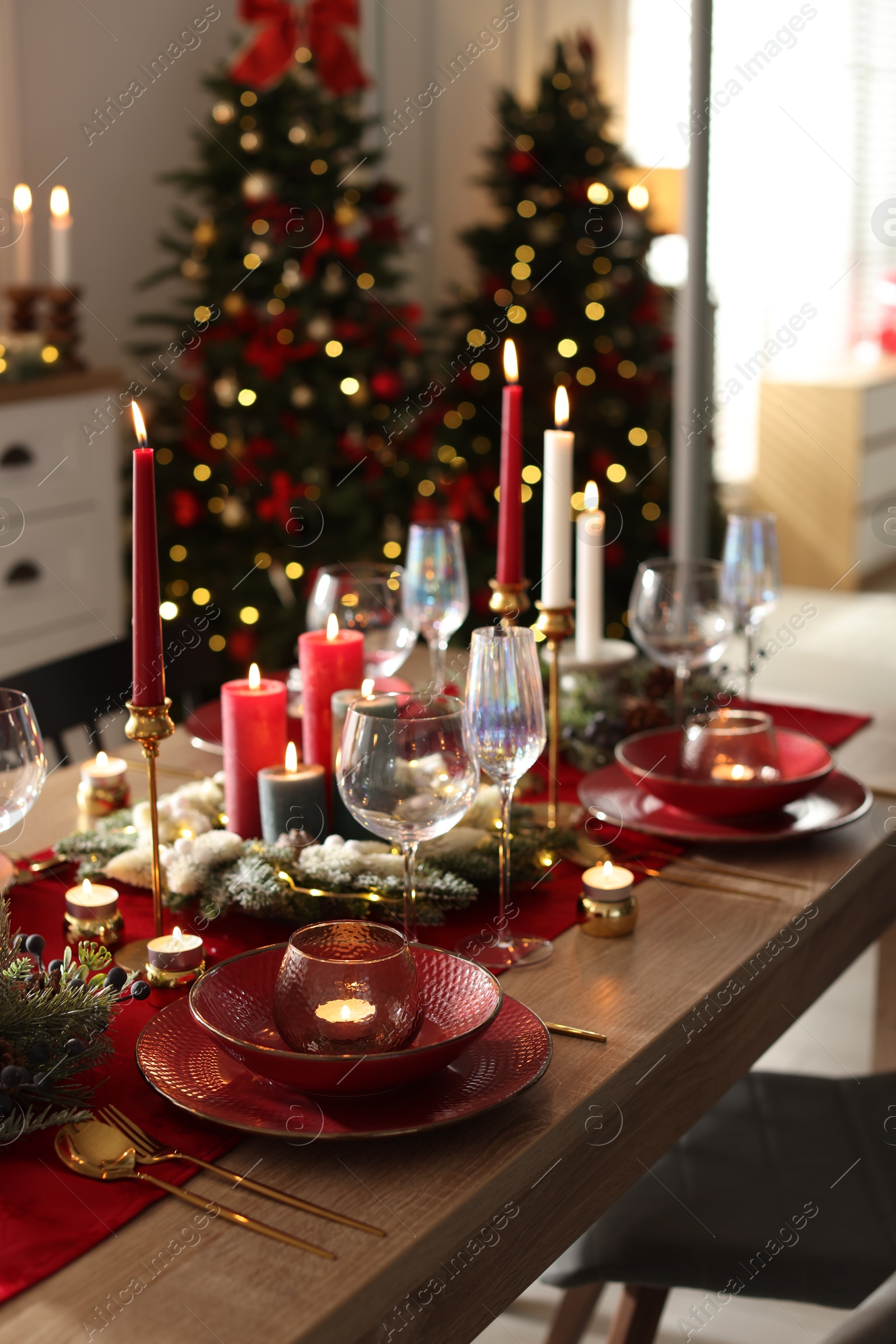 Photo of Christmas table setting with stylish dishware, glasses and burning candles in festive decorated room