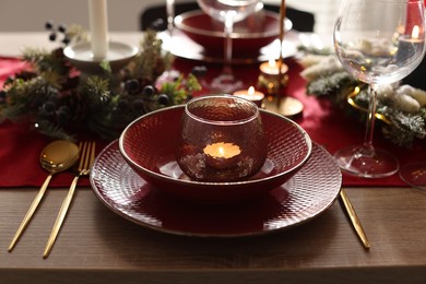 Photo of Christmas place setting with festive decor on wooden table in room, closeup