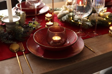 Photo of Christmas place setting with festive decor on wooden table in room, closeup