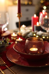 Photo of Christmas place setting with festive decor on wooden table in room, closeup