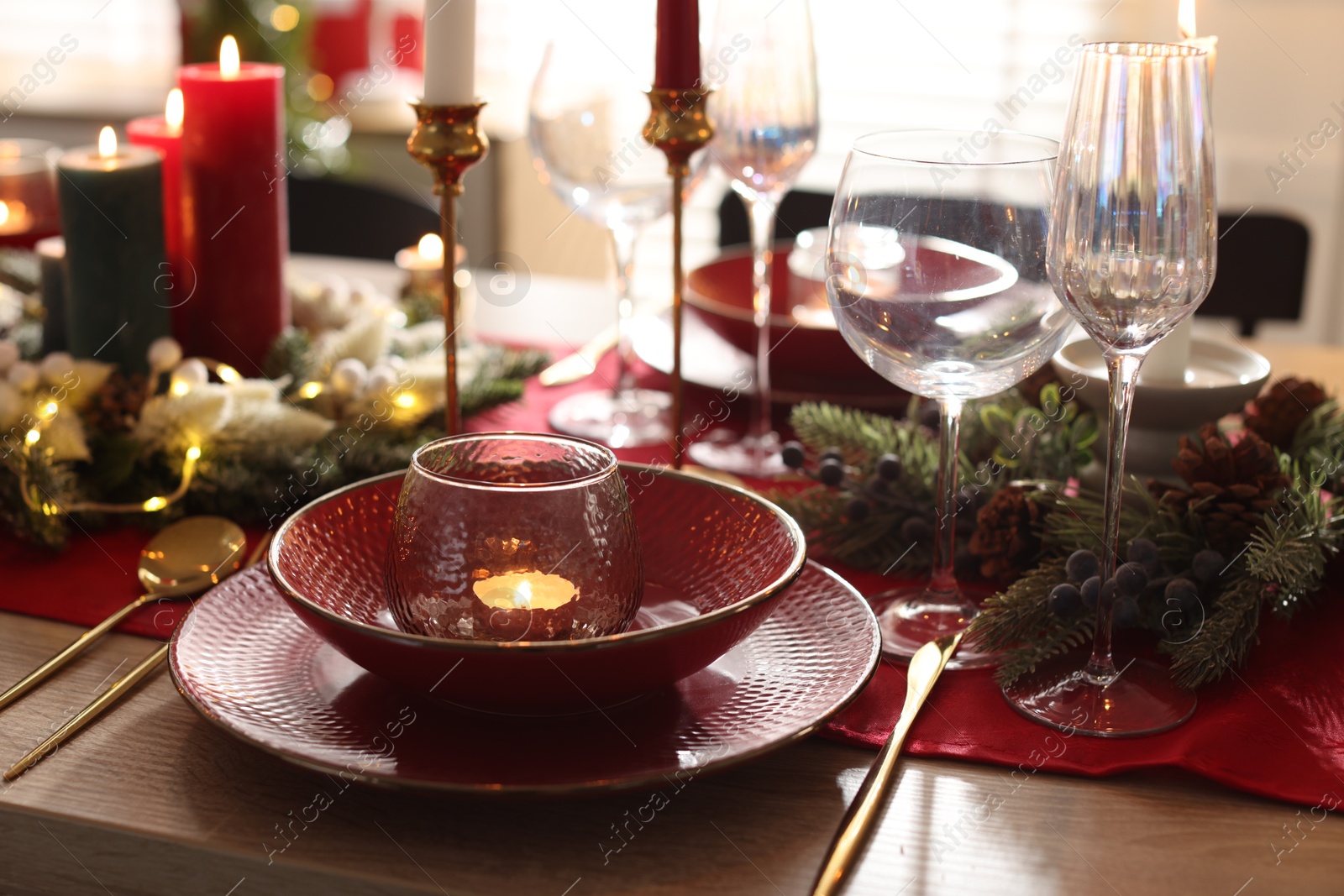 Photo of Christmas place setting with festive decor on wooden table in room, closeup