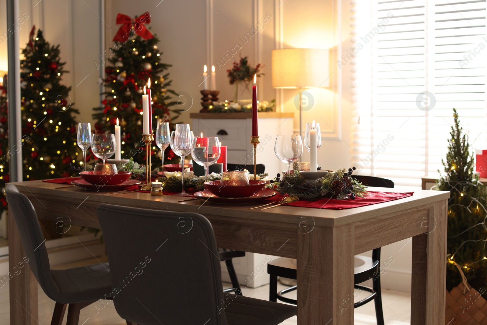 Photo of Christmas table setting with stylish dishware, glasses and burning candles in festive decorated room