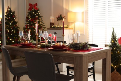 Photo of Christmas table setting with stylish dishware, glasses and burning candles in festive decorated room