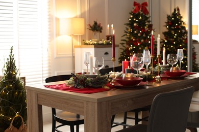 Photo of Christmas table setting with stylish dishware, glasses and burning candles in festive decorated room