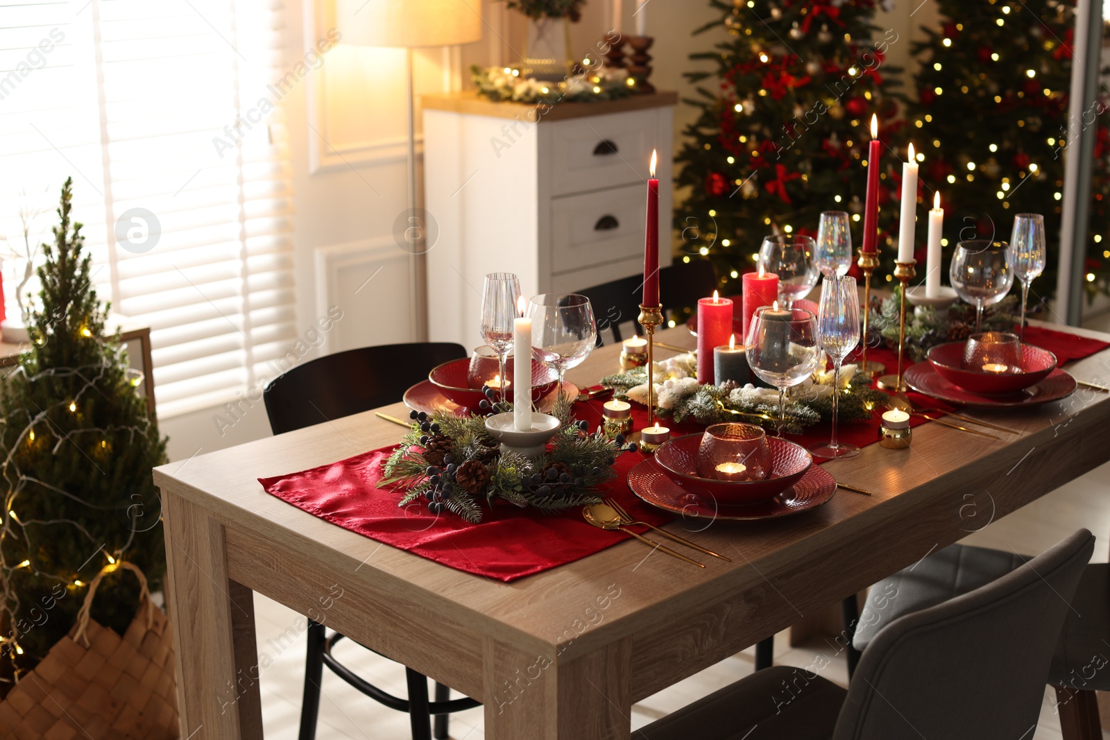 Photo of Christmas table setting with stylish dishware, glasses and burning candles in festive decorated room