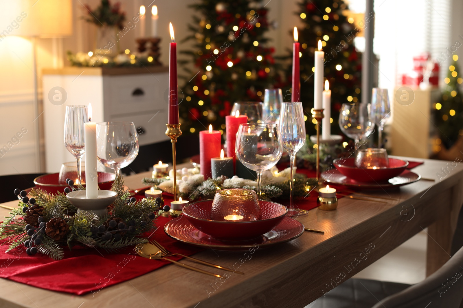 Photo of Christmas table setting with stylish dishware, glasses and burning candles in festive decorated room