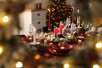 Photo of Christmas table setting with stylish dishware, glasses and burning candles in festive decorated room, selective focus