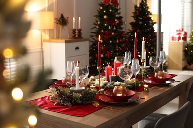 Photo of Christmas table setting with stylish dishware, glasses and burning candles in festive decorated room