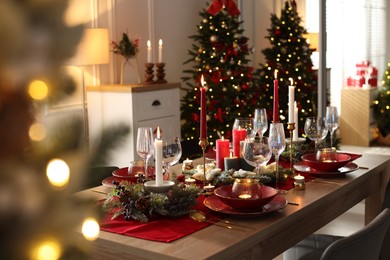 Photo of Christmas table setting with stylish dishware, glasses and burning candles in festive decorated room