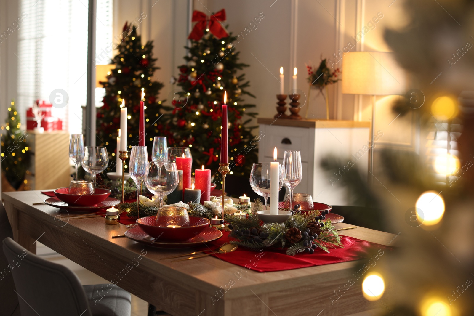 Photo of Christmas table setting with stylish dishware, glasses and burning candles in festive decorated room