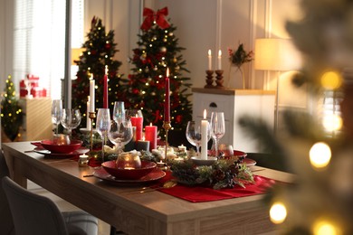 Photo of Christmas table setting with stylish dishware, glasses and burning candles in festive decorated room