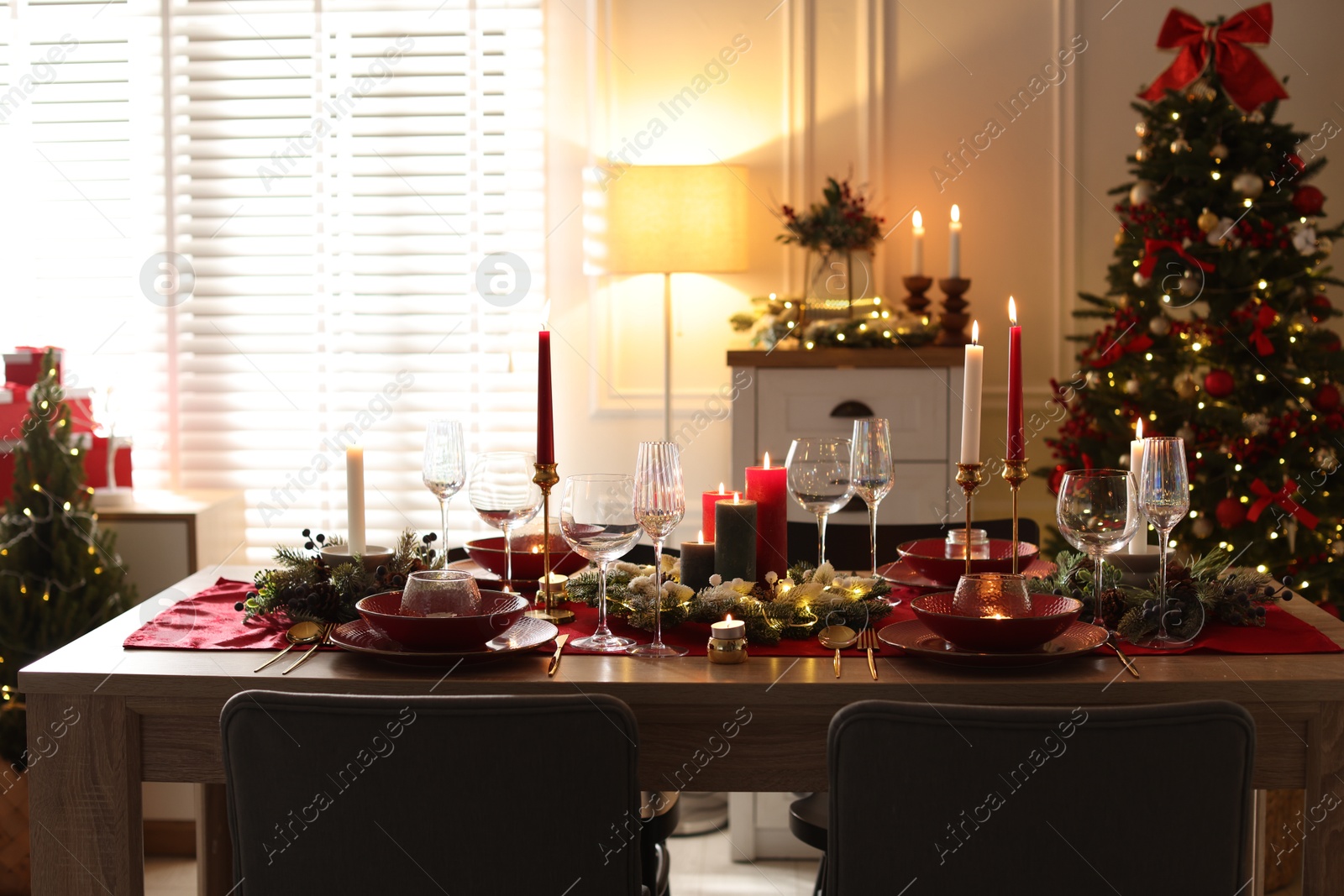 Photo of Christmas table setting with stylish dishware, glasses and burning candles in festive decorated room