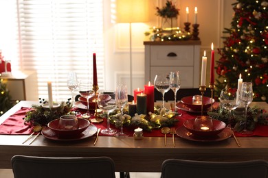 Photo of Christmas table setting with stylish dishware, glasses and burning candles in festive decorated room