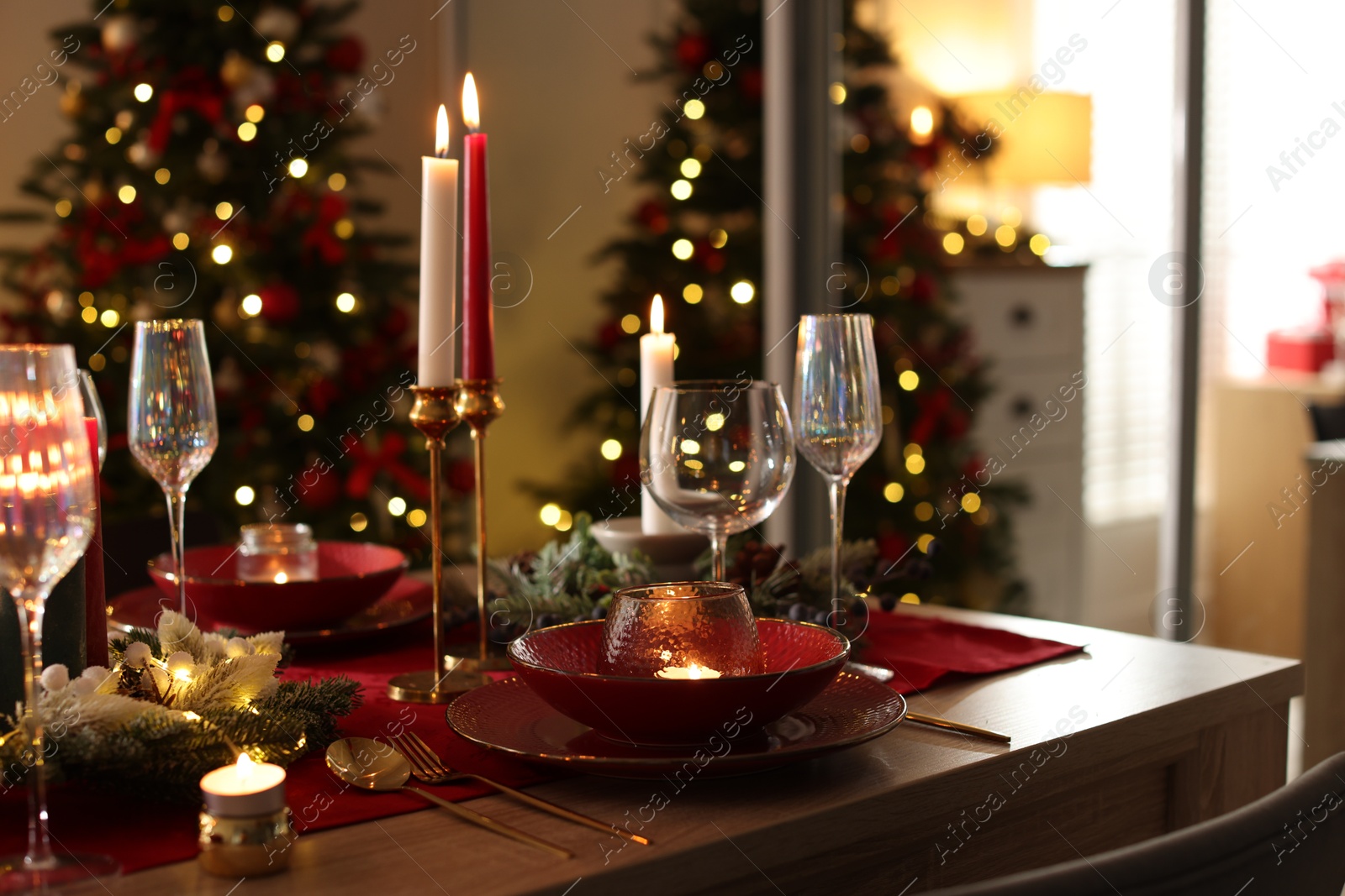 Photo of Christmas table setting with stylish dishware, glasses and burning candles in festive decorated room