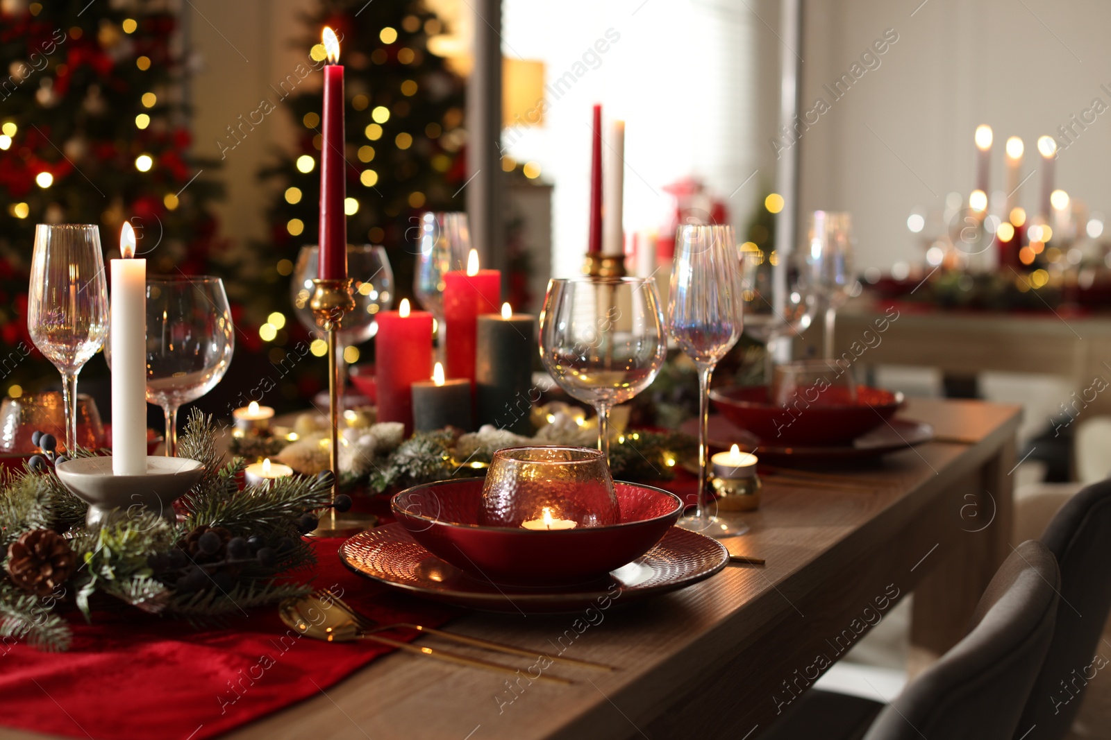 Photo of Christmas table setting with stylish dishware, glasses and burning candles in festive decorated room