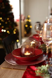 Photo of Christmas place setting with festive decor on wooden table in room, closeup