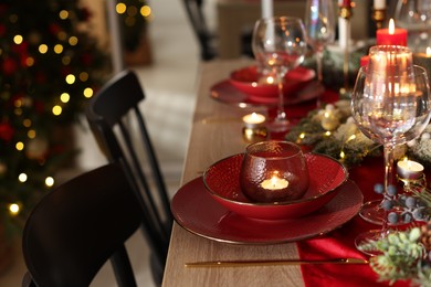 Photo of Christmas place setting with festive decor on wooden table in room, closeup