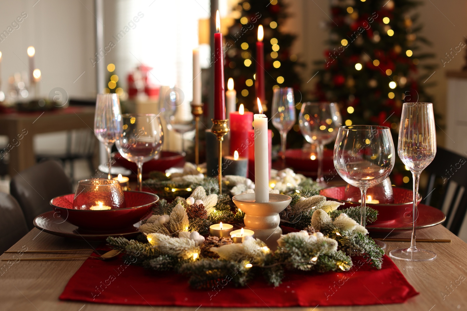 Photo of Christmas table setting with stylish dishware, glasses and burning candles in festive decorated room