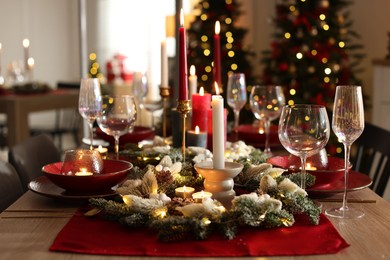 Photo of Christmas table setting with stylish dishware, glasses and burning candles in festive decorated room