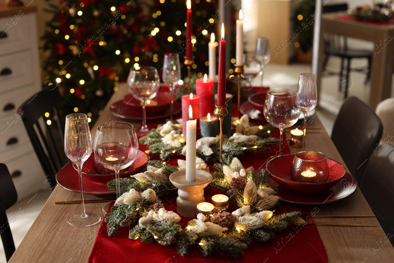 Photo of Christmas table setting with stylish dishware, glasses and burning candles in festive decorated room