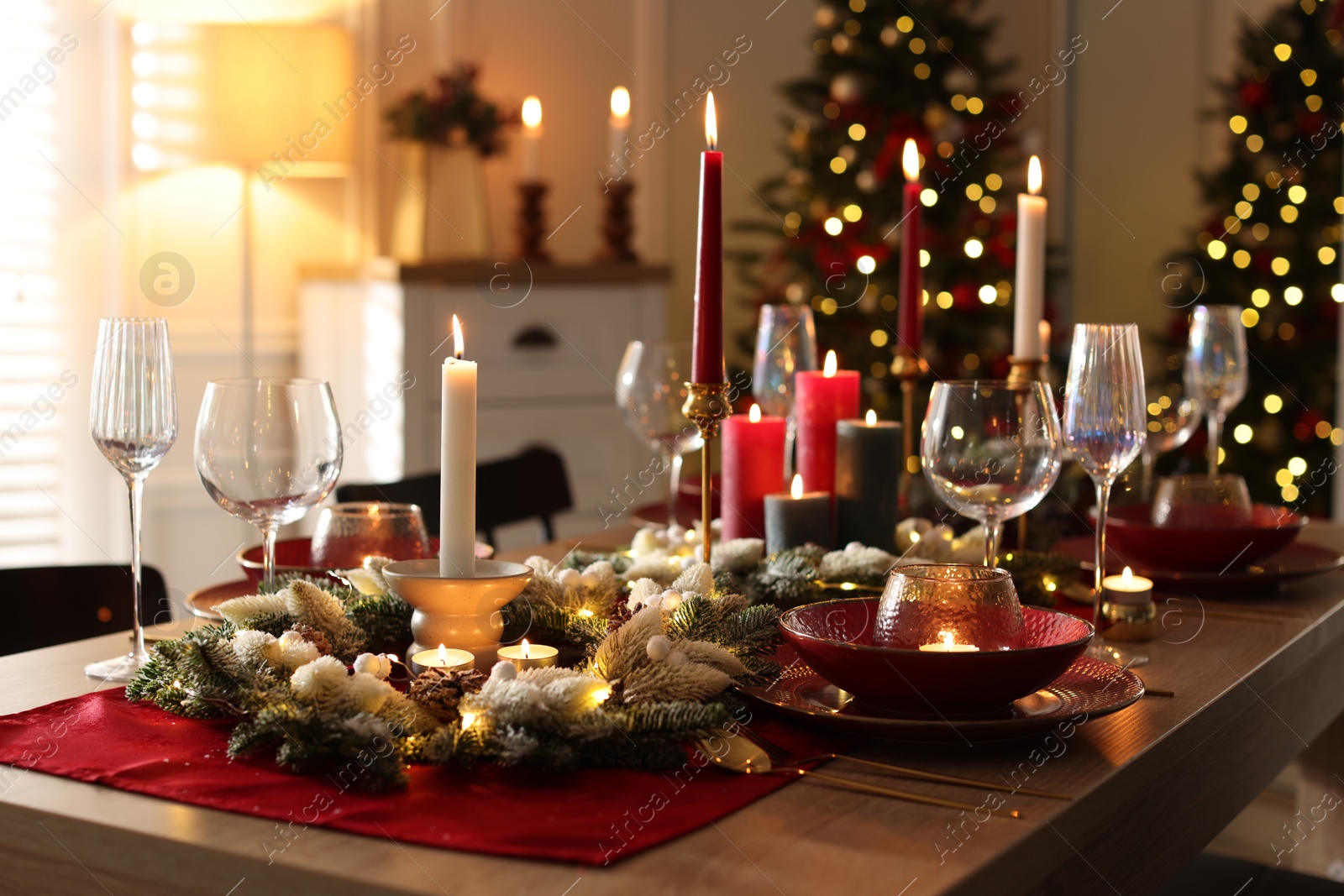 Photo of Christmas table setting with stylish dishware, glasses and burning candles in festive decorated room