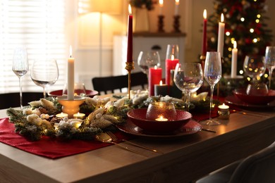 Photo of Christmas table setting with stylish dishware, glasses and burning candles in festive decorated room