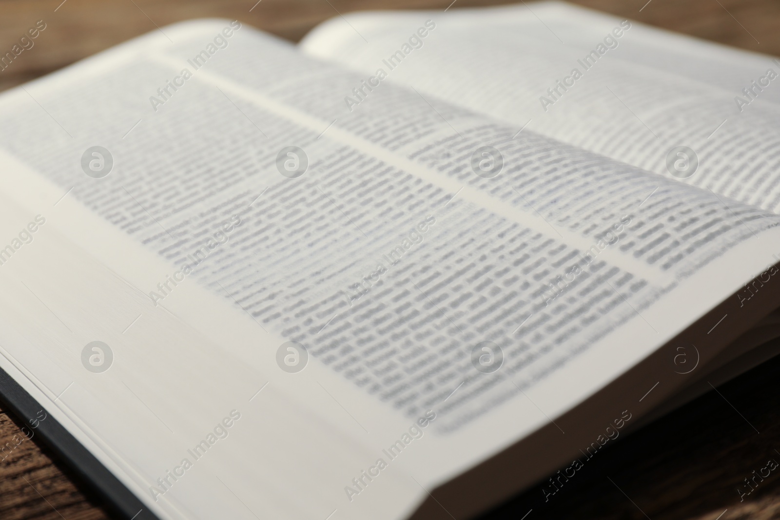 Photo of Open Holy Bible in English language on wooden table, closeup