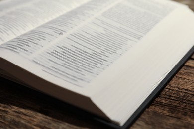 Photo of Open Holy Bible in English language on wooden table, closeup