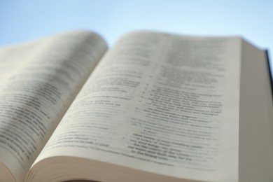 Photo of Open Holy Bible in English language on light blue background, closeup