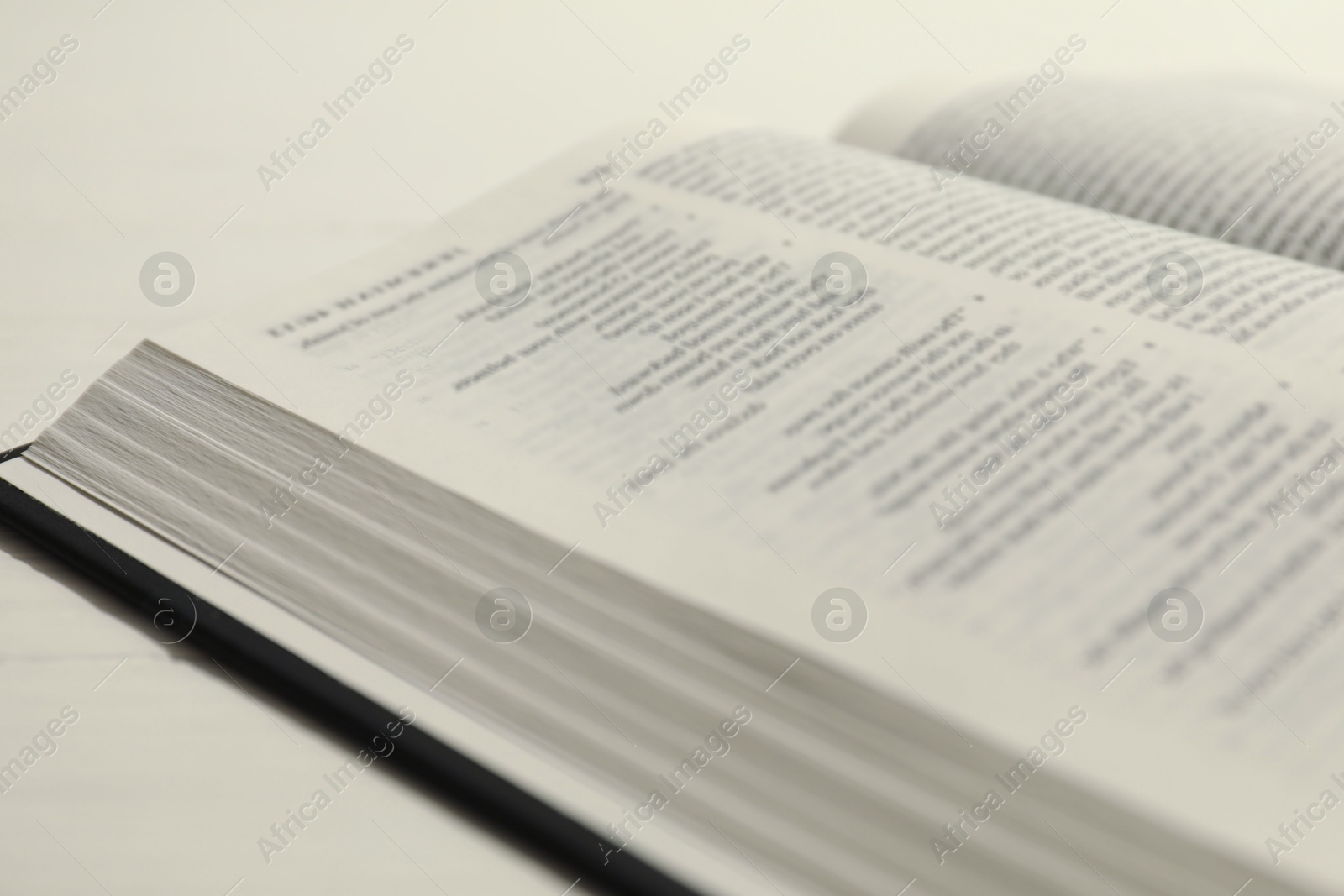 Photo of Open Holy Bible in English language on white table, closeup