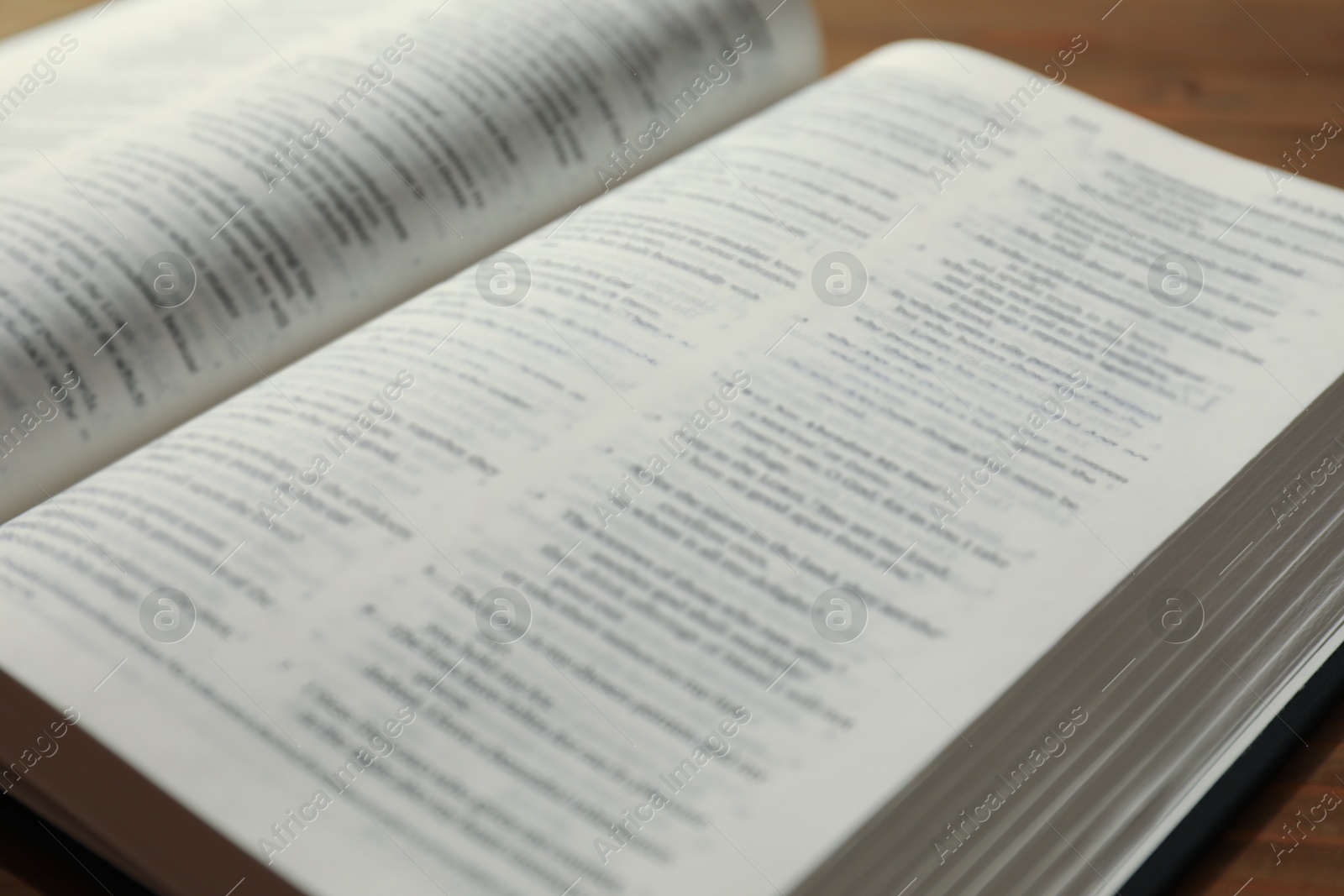 Photo of Open Holy Bible in English language on wooden table, closeup