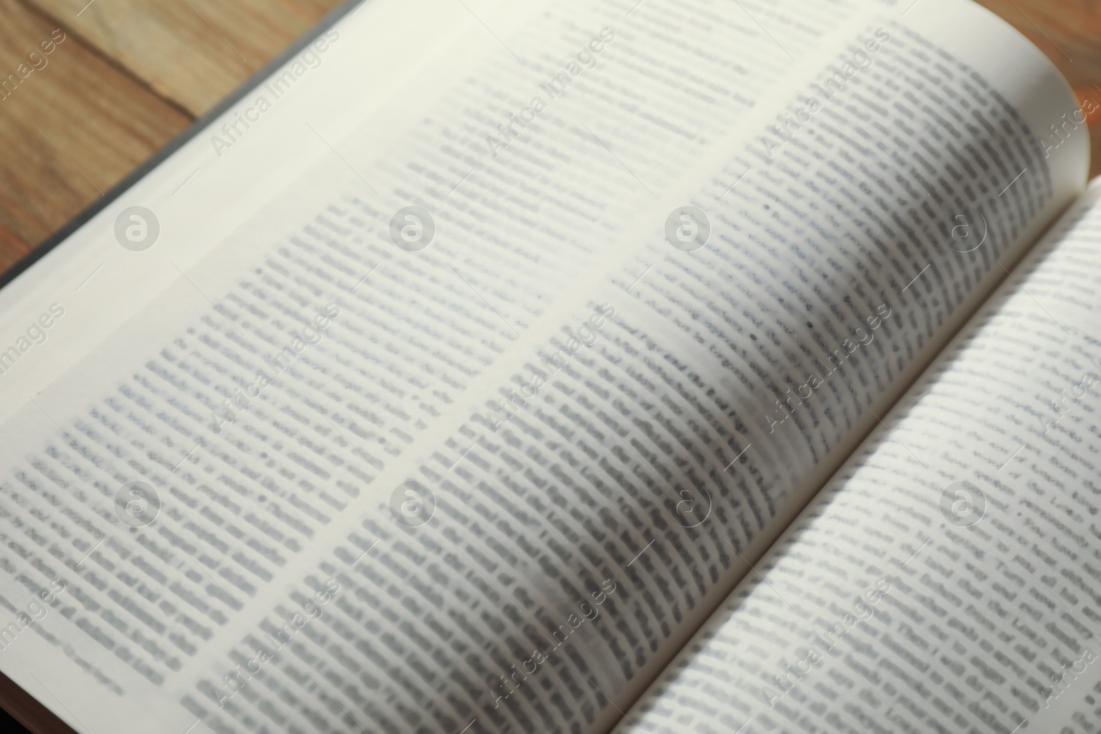 Photo of Open Holy Bible in English language on wooden table, closeup