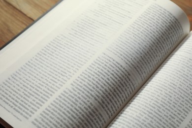 Photo of Open Holy Bible in English language on wooden table, closeup