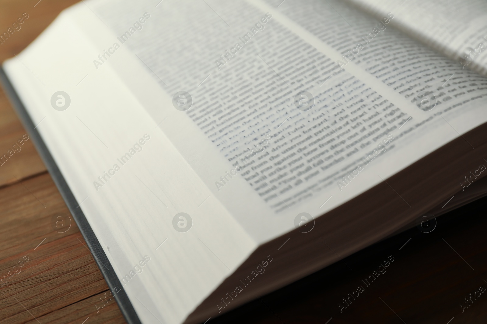 Photo of Open Holy Bible in English language on wooden table, closeup