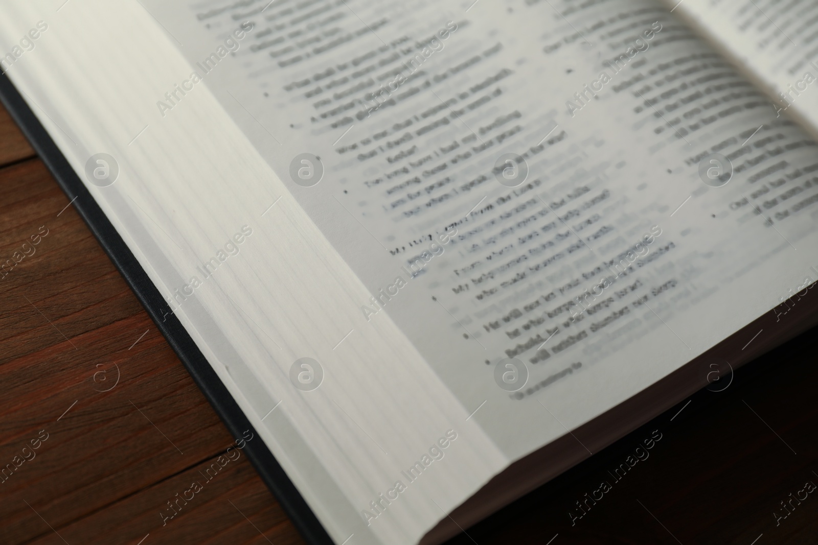 Photo of Open Holy Bible in English language on wooden table, closeup