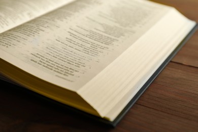 Photo of Open Holy Bible in English language on wooden table, closeup