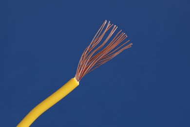 Photo of Yellow stripped electrical wire on blue background, closeup. Space for text