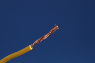 Photo of Yellow stripped electrical wire on blue background, closeup. Space for text