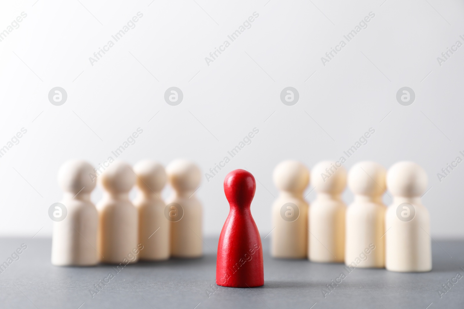 Photo of Human resources concept. Red figure in front of wooden ones on table against light background, closeup. Space for text