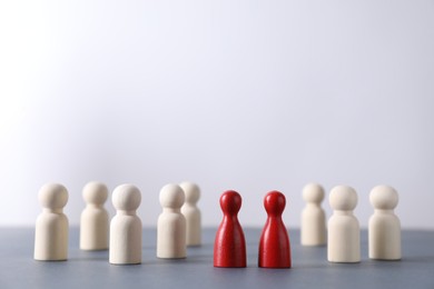 Photo of Human resources concept. Red figures among wooden ones on table against light background, closeup. Space for text