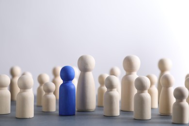 Human resources concept. Blue figure among wooden ones on table against light background, closeup. Space for text