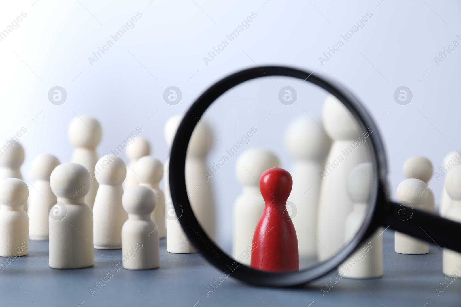 Photo of Human resources concept. Looking at wooden figures through magnifying glass on table against light background, closeup